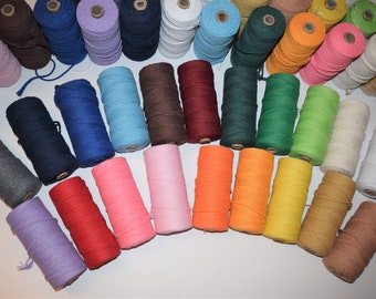 May include: A collection of spools of colorful cotton cord, including shades of blue, red, pink, orange, yellow, green, brown, and gray. The spools are arranged in a semi-circle on a white surface.