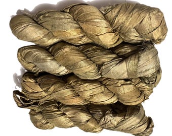 May include: Close-up of several bundles of golden-colored silk ribbon, tightly twisted together. The silk has a subtle sheen, and the bundles are arranged in a layered pattern. The ribbons appear to be handmade.