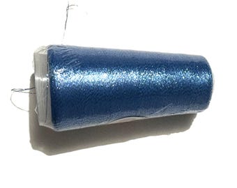 May include: A roll of blue glitter tulle fabric, wrapped in clear plastic. The fabric has a sparkly, textured appearance. The roll is cylindrical and sits horizontally against a white background. Strands of thread are visible.