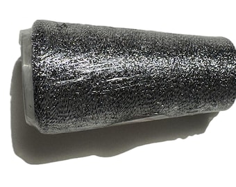 May include: A spool of metallic silver thread, wrapped in clear plastic. The thread has a shiny, glittery appearance, reflecting light. The spool is cylindrical, with a white base and a dark gray thread.