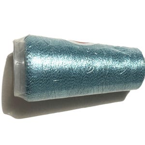 May include: A spool of teal-colored thread, tightly wrapped in clear plastic. The thread has a slight sheen, suggesting a metallic or silk blend. The spool is cylindrical, and the packaging is intact.