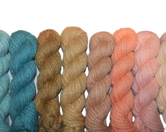 May include: A collection of eight skeins of yarn in various shades of blue, brown, and pink. The yarn is arranged in a row, with the blue skeins on the left and the pink skeins on the right.