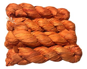 May include: Braided orange silk ribbon, tightly woven and textured. The silk has a slight sheen, and the color is a warm, vibrant orange. A small white string is tied at one end. This ribbon is suitable for crafts and embellishments.