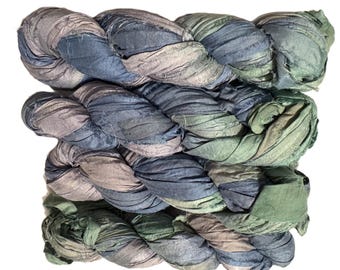 May include: Braided yarn in shades of blue, green, and gray. The yarn appears to be made of a textured fabric, possibly silk or a similar material. The colors blend together, creating a soft, natural look. Ideal for crafting projects.