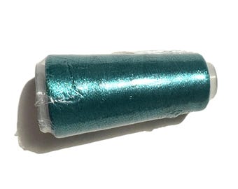May include: A spool of teal-colored thread, wrapped in clear plastic. The thread has a metallic sheen, reflecting light. The spool has white end caps. Ideal for sewing, embroidery, or other craft projects.