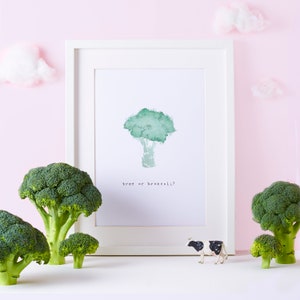 May include: A white framed print with a watercolor illustration of a broccoli tree. The text "tree or broccoli?" is printed below the illustration. There are three broccoli florets in the foreground, and a toy cow in front of the print.