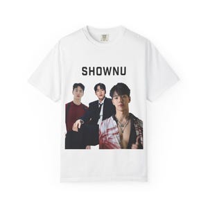 May include: A white short-sleeved t-shirt featuring a graphic print of the name SHOWNU in black capital letters above a photograph of three individuals. The image shows one person in a maroon sweater, one in a black suit, and one in a patterned shirt.