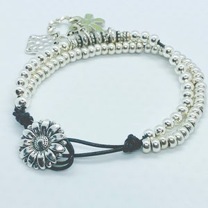 0179 Double layer gray leather bracelet made with silver plated beads and a three charms with a flower clasp.