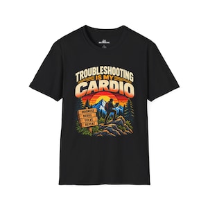 Könnte beinhalten: Ein schwarzes Kurzarm-T-Shirt mit einer Grafik einer Person auf einem Berg mit Laptop. Der Text "TROUBLESHOOTING IS MY CARDIO" steht über einem Sonnenuntergang, daneben ein Holzschild mit der Aufschrift "DIAGNOSE, DEBUG, SOLVE, REPEAT" und Tannenbäumen.