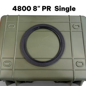 May include: An olive green rectangular hard-shell protective case featuring a black circular ring centered on the lid. The text 4800 8" PR Single is printed in black above the case. The case has a ribbed exterior with four recessed corner points.