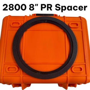 May include: A black circular spacer resting on a bright orange rectangular hard-shell case. The text 2800 8" PR Spacer is printed in black above the case. The spacer has a flat, textured surface and a uniform ring shape.