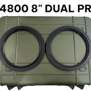 May include: An olive green rectangular hard-shell case with two black circular rings placed on top. The text 4800 8" DUAL PR is printed in black above the case. The case features a ribbed exterior design with reinforced corners and edges.