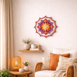May include: A circular wall hanging made of colourful yarn in shades of purple, orange, and yellow, featuring a geometric star pattern. The piece is constructed with a central star motif radiating outward into concentric layers of vibrant thread.