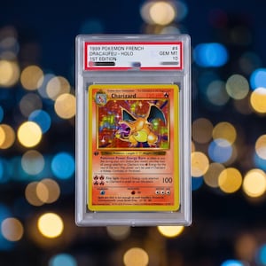 May include: A 1999 Pokemon 1st Edition Charizard trading card encased in a clear protective PSA slab. The card features a holographic illustration of the orange dragon-like creature, with text including 120 HP and the name Charizard.