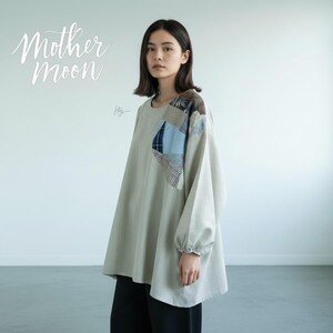 May include: A light gray long-sleeve tunic featuring a patchwork design on the upper left chest with blue, brown, and patterned fabric squares. The garment has a round neckline, loose fit, and elasticized cuffs. The text Mother Moon is visible.