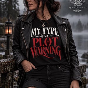 May include: A black t-shirt featuring the white and red text "MY TYPE is a PLOT WARNING" printed on the front. The shirt is worn under a black leather jacket with silver hardware, paired with black distressed jeans and a black knit beanie cap.