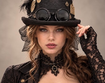 Può includere: Un cilindro nero decorato con ingranaggi dorati, piume scure e occhiali neri. Il cappello presenta un velo in pizzo nero ed è abbinato a un girocollo in pizzo nero con una pietra centrale scura e un indumento a maniche lunghe in pizzo.