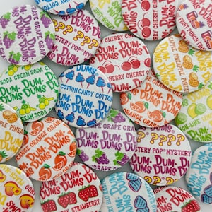 May include: A collection of round Dum-Dums lollipops in various colourful wrappers featuring flavours like grape, cherry, cotton candy, orange, pineapple, and strawberry, with printed text identifying each flavour and the brand name.