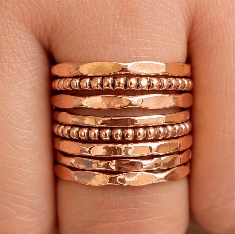 A close-up image of a person's hand wearing multiple rings stacked on top of each other.
