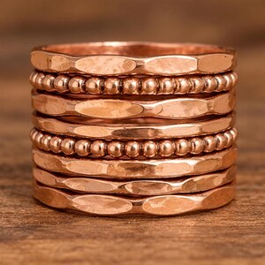 A stack of copper-colored metal rings or bracelets arranged on a wooden surface.