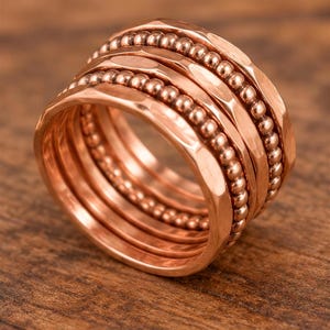 A close-up image of a copper-colored ring with a textured surface, featuring a series of concentric bands with small beads.
