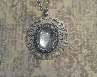 May include: A silver pendant necklace with a delicate filigree design. The pendant features a clear glass cabochon with a floral pattern.