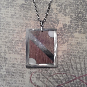 May include: A silver chain necklace with a rectangular pendant made of wood, metal, and white material. The pendant has a wood grain pattern and a silver stripe running diagonally across it. The pendant is surrounded by a silver border.