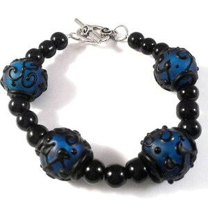 May include: A blue and black bracelet with a toggle clasp. The bracelet features blue beads with black floral designs and black beads.
