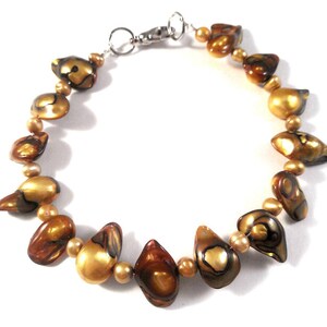 May include: A gold and brown shell bead bracelet with a silver clasp. The beads are irregular in shape and have a pearlescent finish.