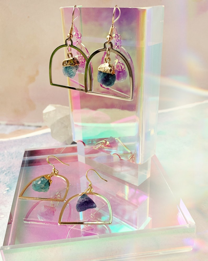 Pode incluir: Brincos de argola de ouro com uma pedra de cristal azul-esverdeada e roxa pendurada em cada argola.
