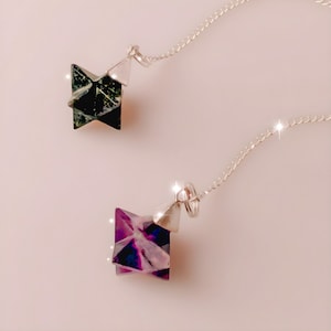 Könnte beinhalten: Zwei silberne Ketten mit Kristallpendeln. Das obere Pendel ist ein dunkelgrüner sternförmiger Kristall. Das untere Pendel ist ein lila und blauer sternförmiger Kristall.