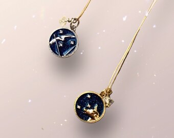 Puede incluir: Dos collares de oro con colgantes azules y dorados. Los colgantes son redondos y tienen un diseño de noche estrellada. Un colgante presenta un pájaro plateado, el otro presenta un animal dorado.