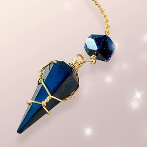May include: A gold chain with a blue crystal pendant. The pendant is wrapped in gold wire and has a faceted shape. The crystal is a dark blue color with a hint of green.