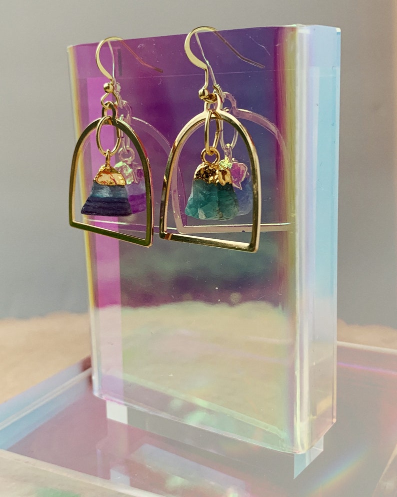 Pode incluir: Brincos de argola dourados com uma pedra de cristal roxa e verde pendurada em cada argola.