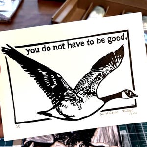 Peut inclure: Une impression rectangulaire blanche présentant une illustration en linogravure à l'encre noire d'une oie en vol. Le texte "You do not have to be good." est imprimé en noir au-dessus de l'oie. L'impression inclut le texte manuscrit "Wild Geese" et "2020".