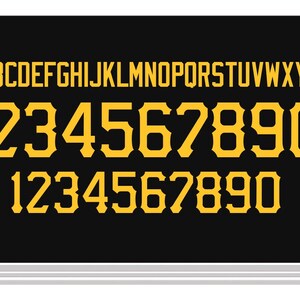 May include: A black rectangular sheet featuring a full set of yellow capital letters from A to Z in a sans-serif font, followed by two rows of yellow numbers from 1 to 0 in a bold, serif-style athletic font with distinct notched edges.