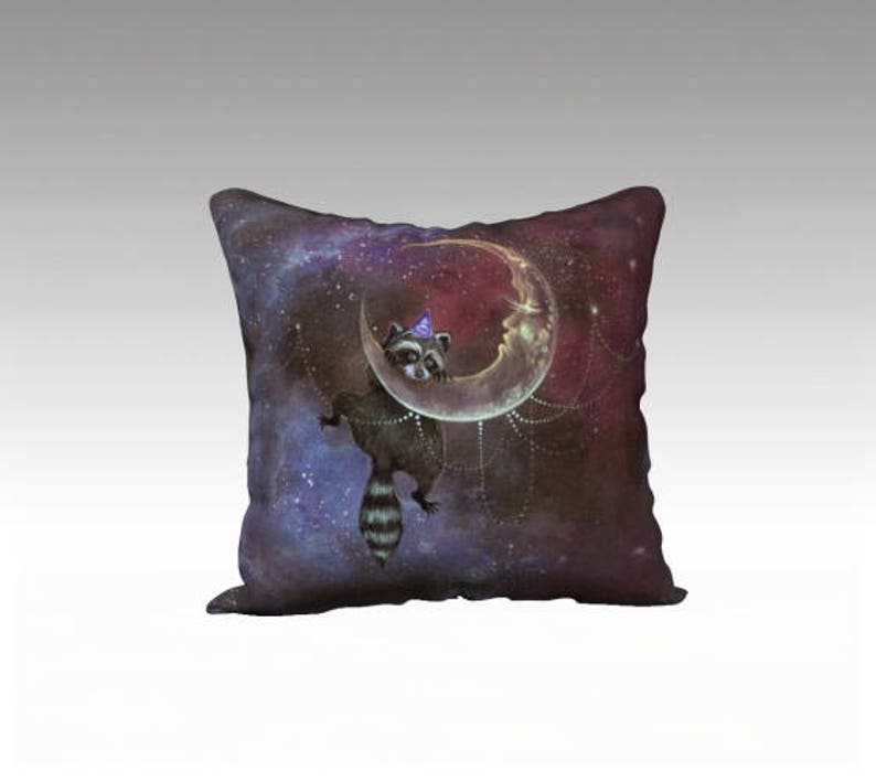 May include: Square cushion with a fantasy design of a raccoon in a party hat on a crescent moon. The background is a dark, starry night sky in purple, blue, and red hues. The raccoon has a striped tail and is hanging from the moon.