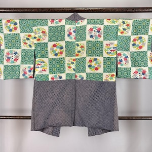 May include: A haori jacket featuring a top section with a checkered pattern of green geometric shapes and white squares containing colourful floral circles. The bottom section and sleeve ends are dark blue with a fine, dense white dot pattern.