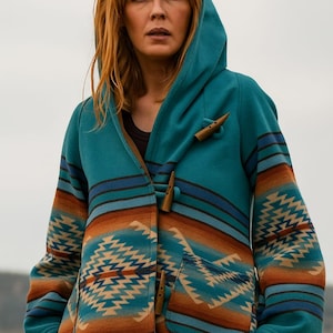 May include: A hooded jacket in a vibrant teal color featuring a horizontal geometric pattern in shades of orange, brown, and dark blue. The garment includes two large front pockets and is fastened with three brown wooden toggle closures.