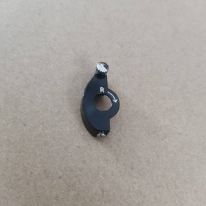 Puede incluir: Pomo de cambio de marchas de plástico negro con una perilla plateada y una 'R' blanca y una flecha que indica la dirección de rotación.