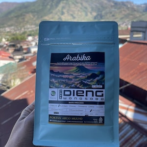 May include: A light blue, rectangular coffee pouch featuring a label with the text Arabika, Dieng Wonosobo, and Poktan Argo Mulyo. The label displays a colorful mountain landscape illustration, a 250 gram weight indicator, and various checkboxes.