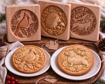 May include: Three square wooden cookie molds featuring carved designs of a cardinal, a hedgehog, and a dachshund, accompanied by two round cookies embossed with the cardinal and dachshund designs, all displayed on a wooden tray.