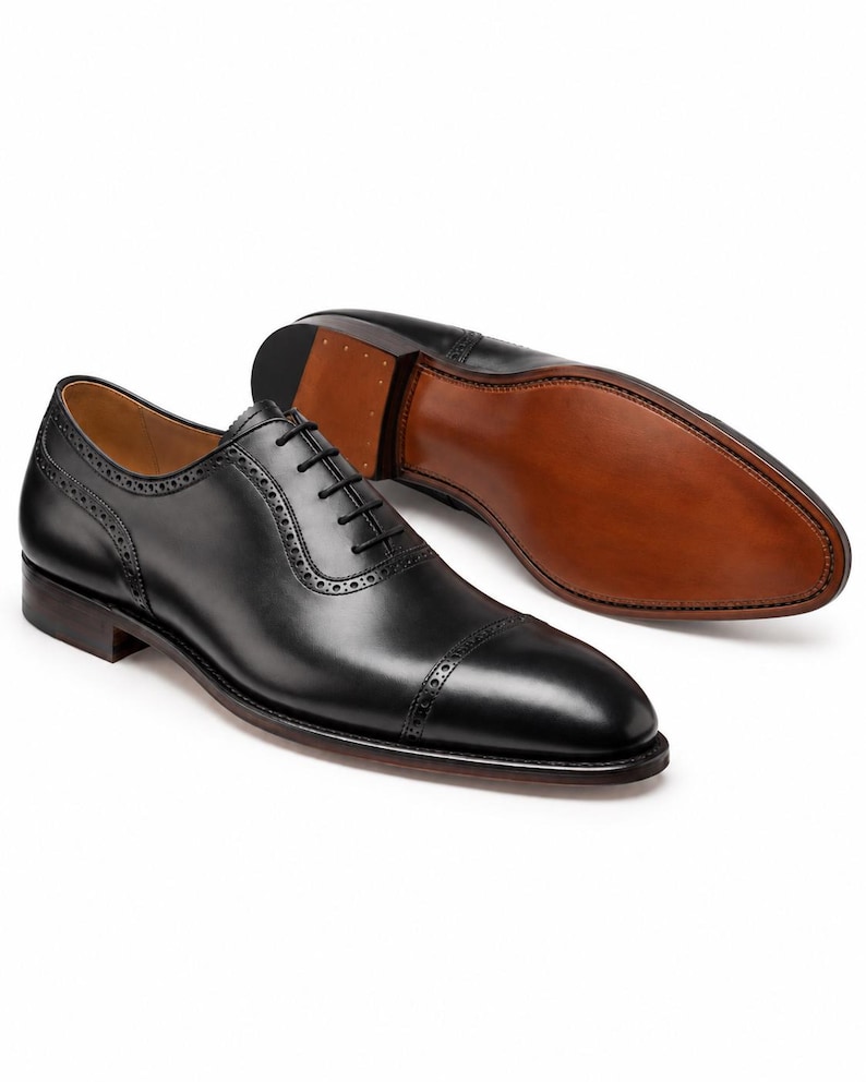 Men’s black leather Oxford shoes with stitched leather sole, cap toe brogue detailing and handcrafted formal dress-shoe finish.
