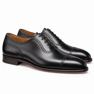 Side view of men’s black cap toe Oxford shoes featuring polished leather, brogue trim, sleek profile and elegant dress-shoe construction.
