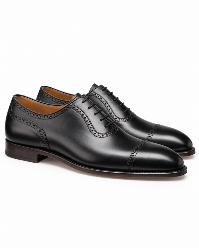 Side view of men’s black cap toe Oxford shoes featuring polished leather, brogue trim, sleek profile and elegant dress-shoe construction.