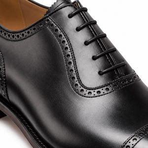 Close-up of men’s black Oxford dress shoe showing closed lacing, brogue perforations and smooth polished leather upper.