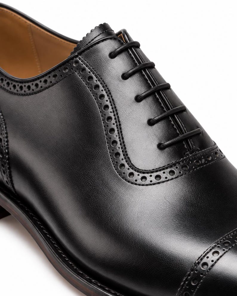 Close-up of men’s black Oxford dress shoe showing closed lacing, brogue perforations and smooth polished leather upper.