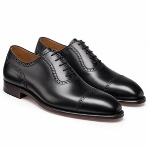 Men’s black leather Oxford dress shoes with punched cap toe, brogue detailing, closed lacing and classic formal silhouette.