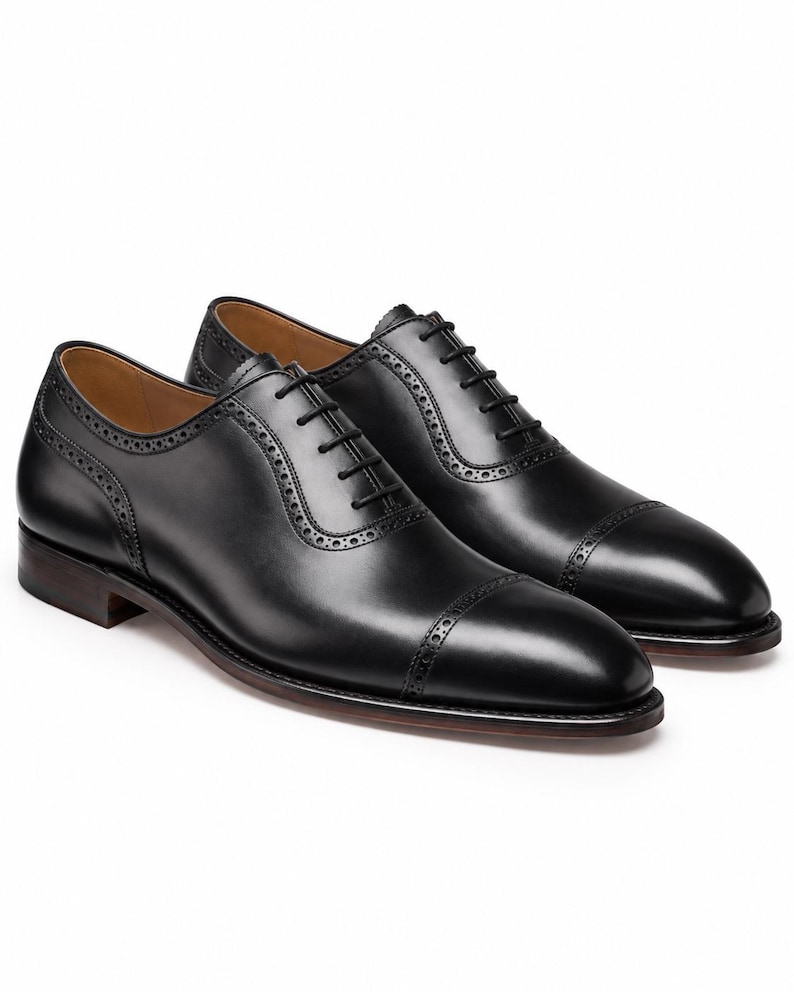 Men’s black leather Oxford dress shoes with punched cap toe, brogue detailing, closed lacing and classic formal silhouette.