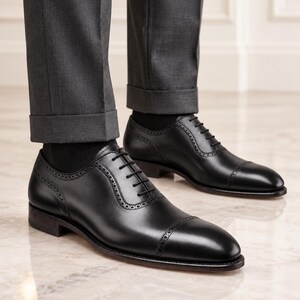 Man wearing black leather cap toe Oxford shoes with tailored trousers, ideal for weddings, business meetings and formal occasions.